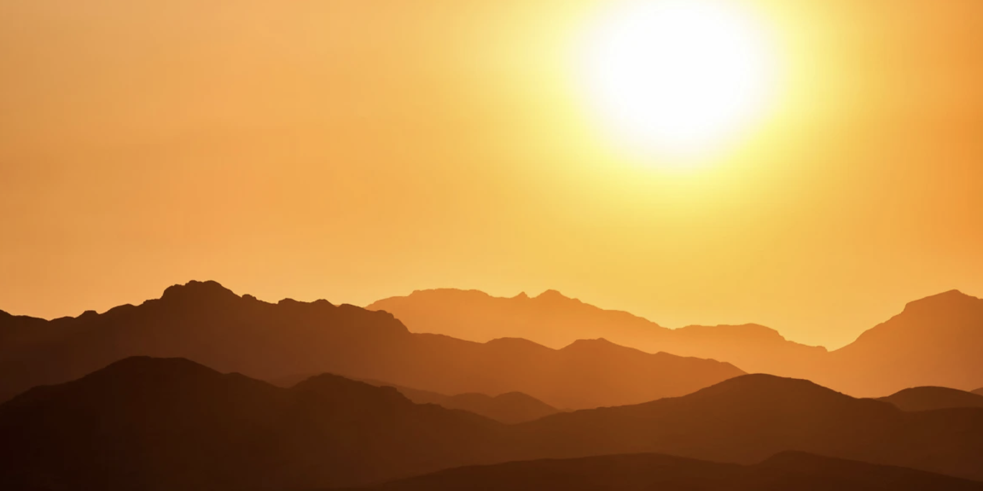 A sepia-toned landscape where we see a hazy sun over a mountainous horizon