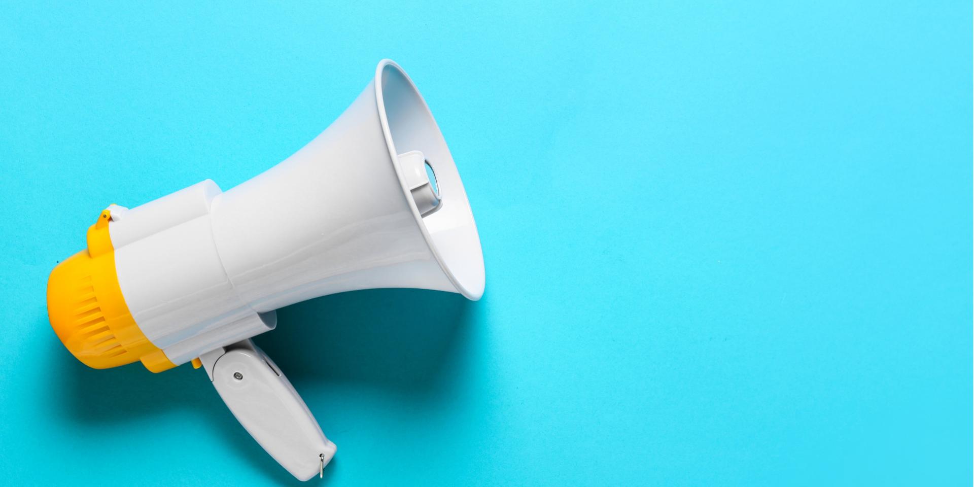 A white and yellow megaphone laying on its side against a teal background