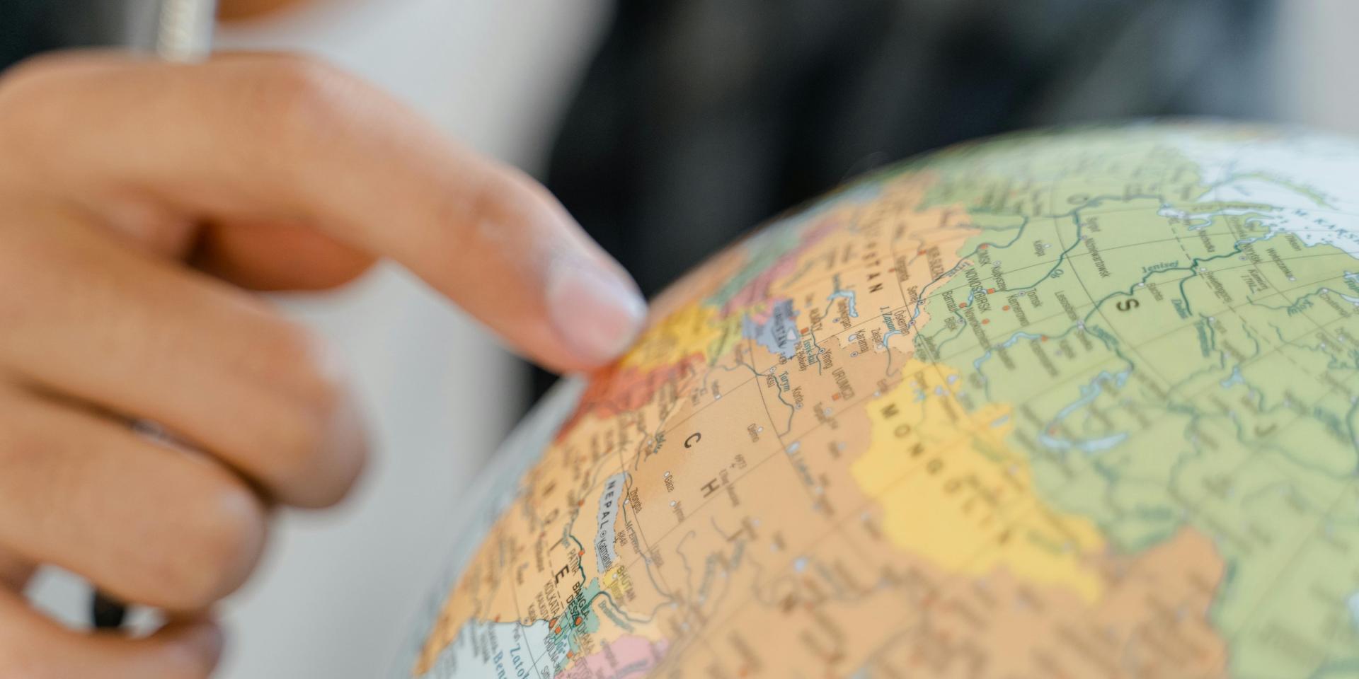 A person pointing to a spot on a colorful world globe