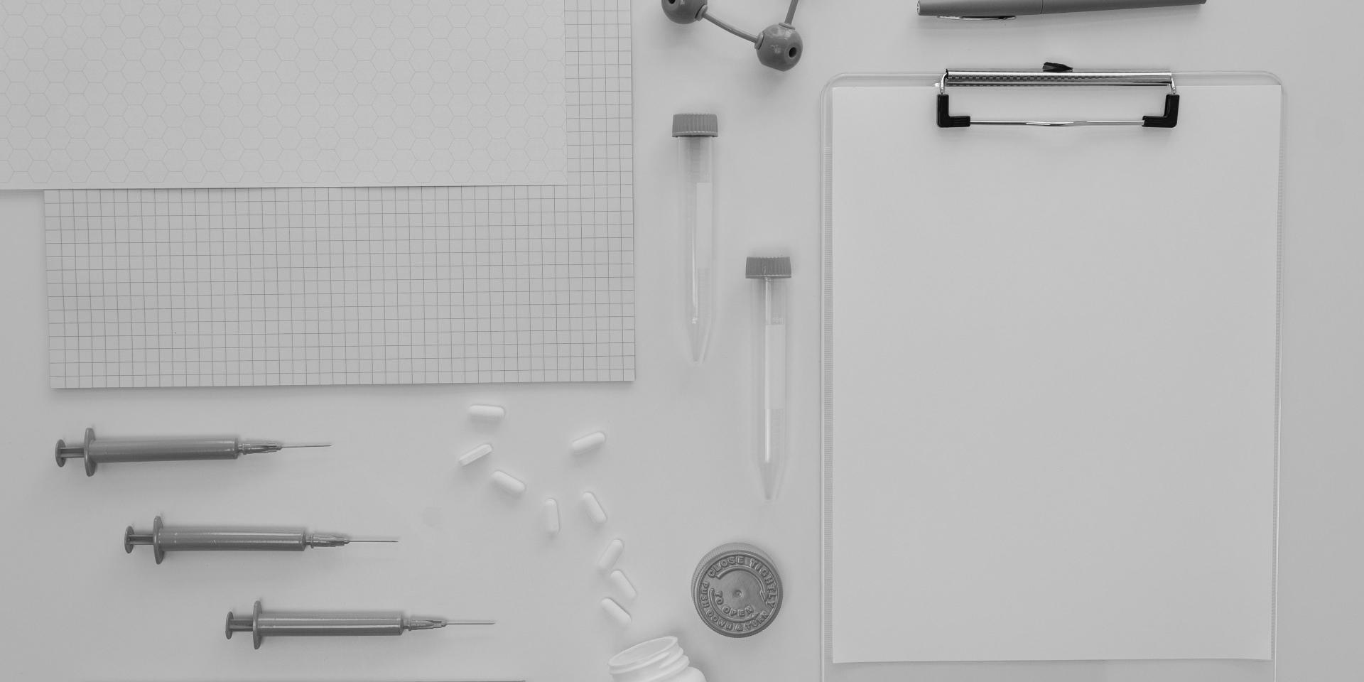 A marker, syringes, test tubes, atom figure, pills, pill bottle, clipboard and papers on a white table