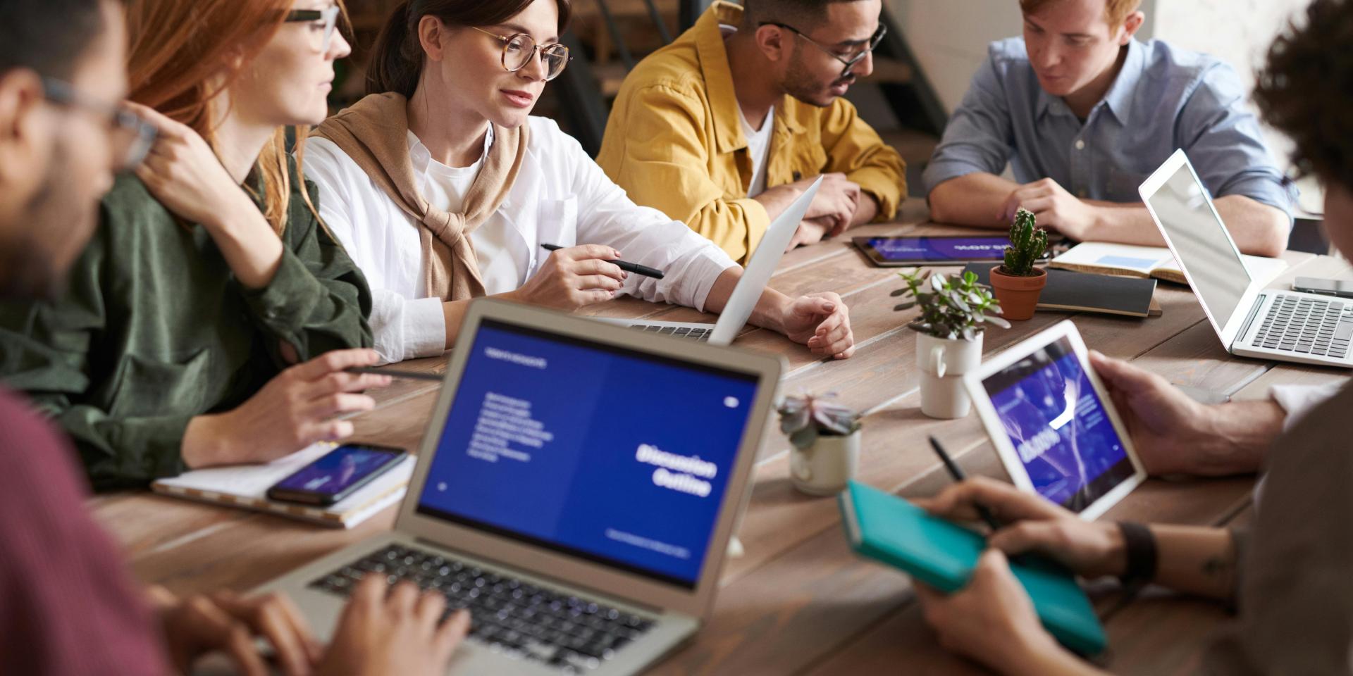 A group of people sits at a table using laptops and collaborating
