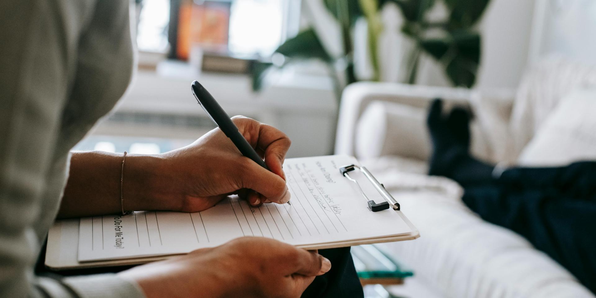 A person writes on paper using a pen and clipboard