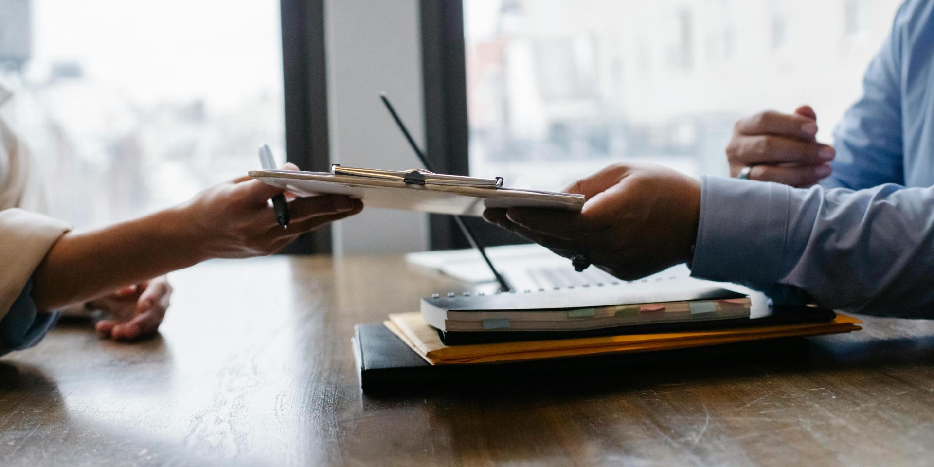 One person passes a clipboard to another across a desk
