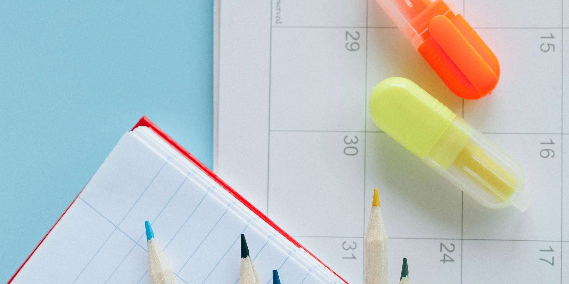 Notebook paper, pencils and highlighters sit on blue desk surface