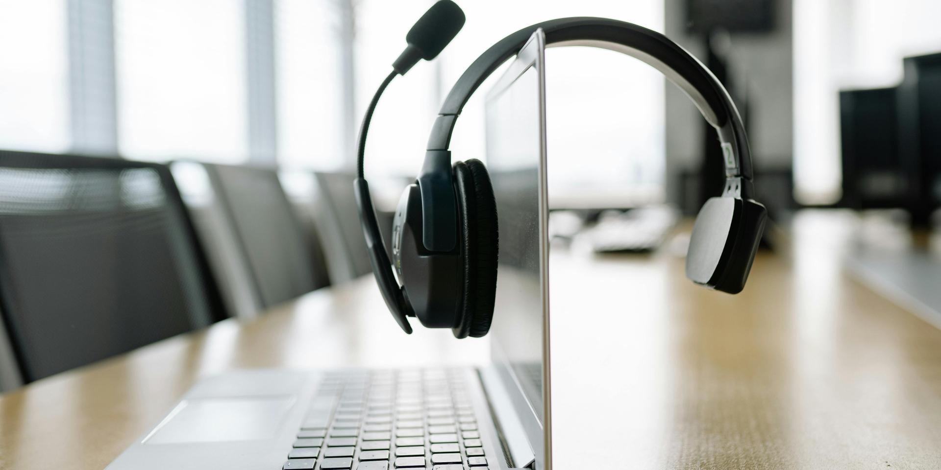 A headset hangs on a laptop, which sits on a conference table