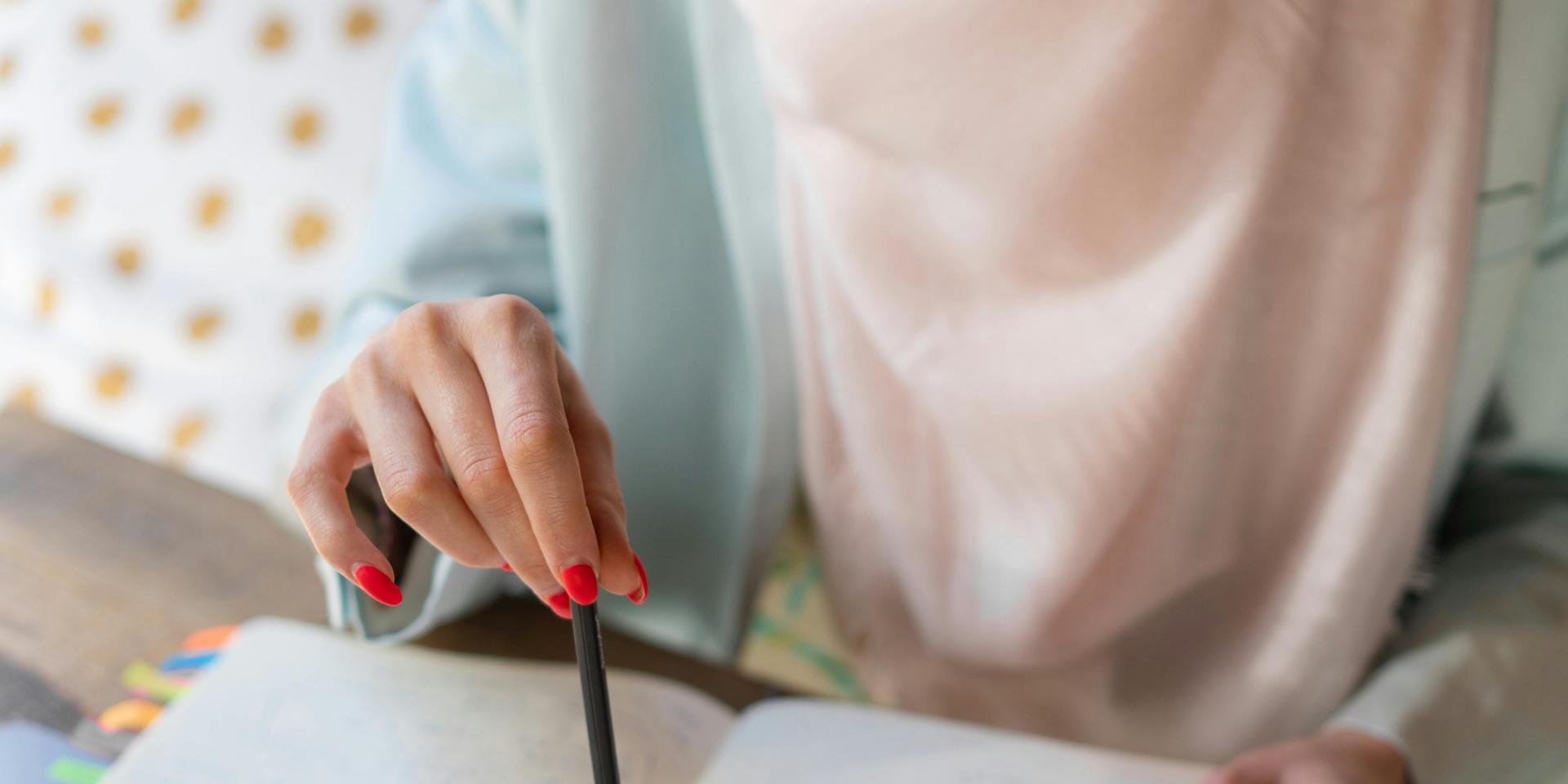 A person consults a notebook, pointing to its pages with a pencil