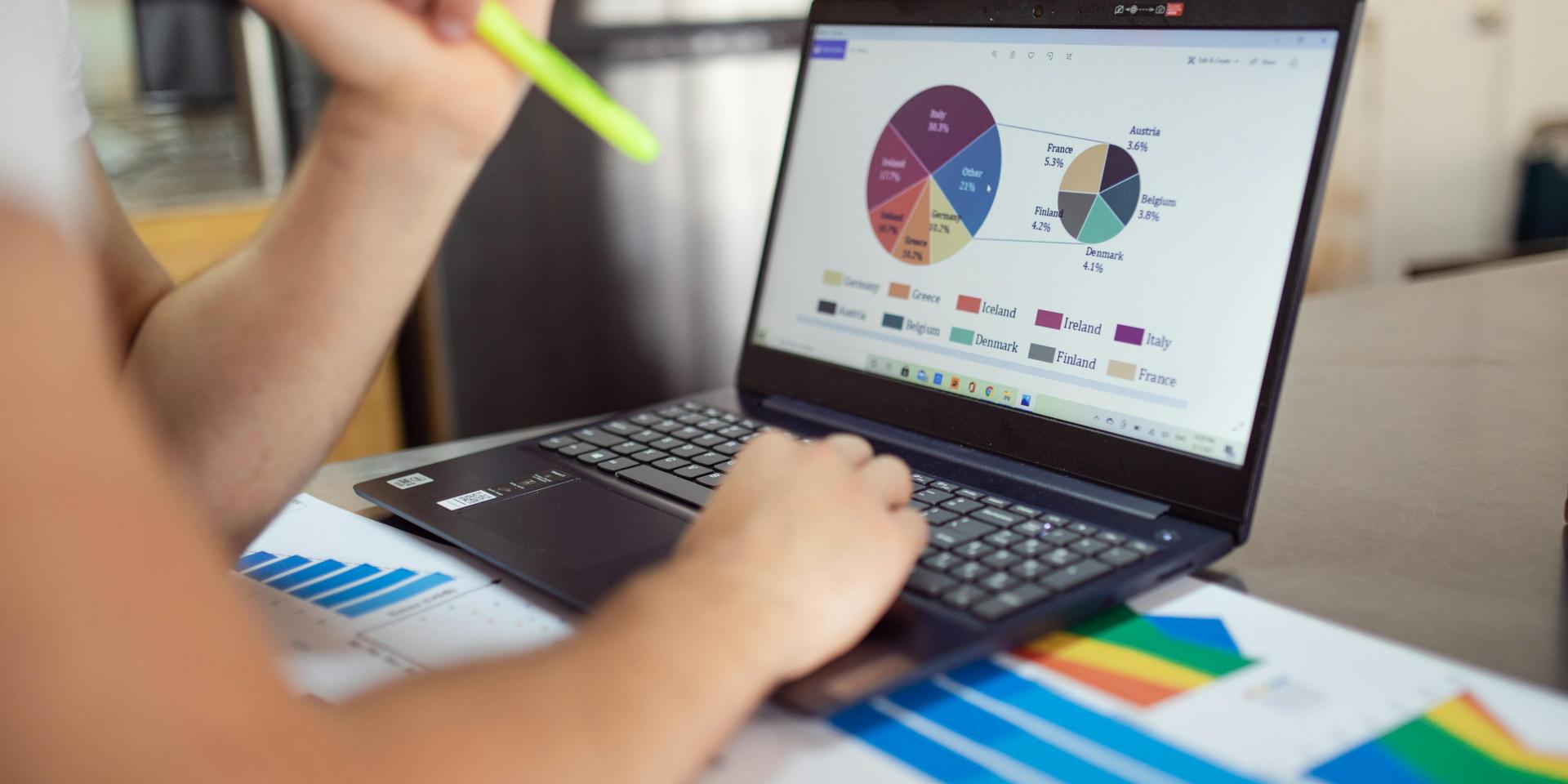 A person, seated, works on a laptop, consulting pie graphs
