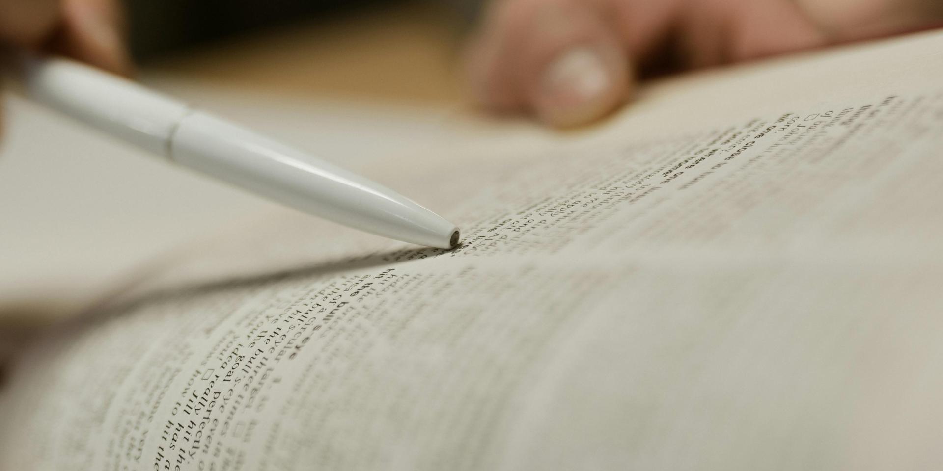 A person using a writing implement to point to a page in a book