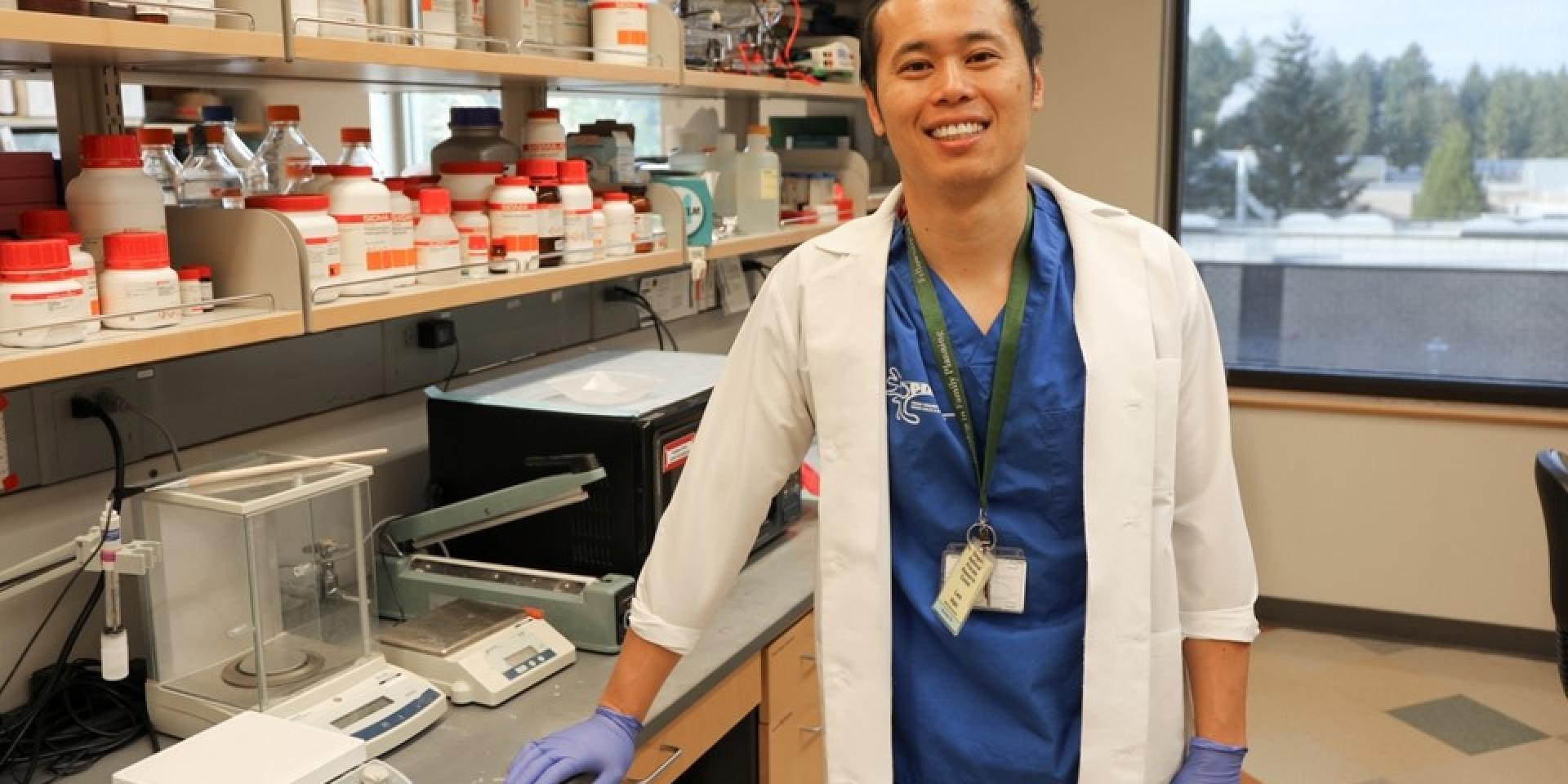 Man in a whote coat and blue scrups stands in a laboratory