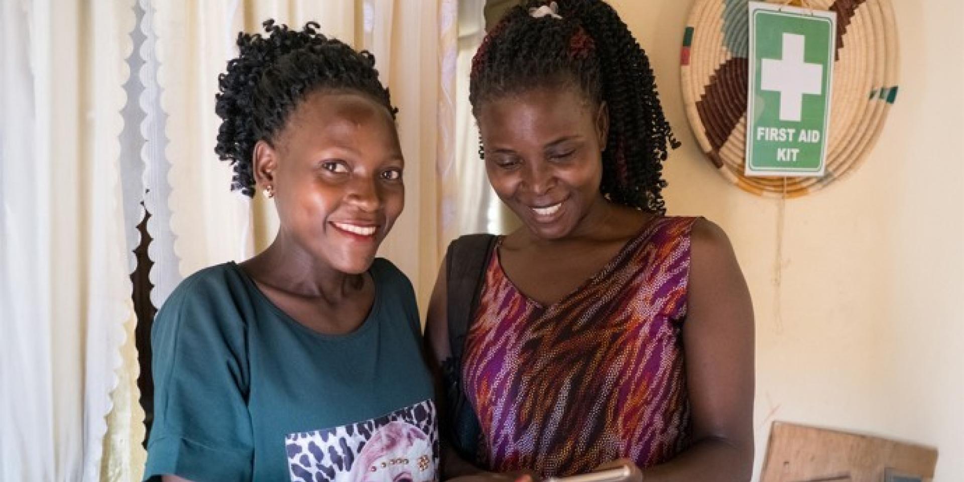 Two black women standing next to each other smiling, one with a teal tshirt and the other with a pink tank top