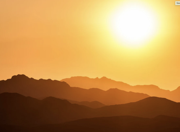 A sepia-toned landscape where we see a hazy sun over a mountainous horizon