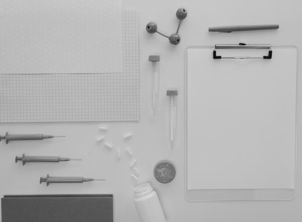 A marker, syringes, test tubes, atom figure, pills, pill bottle, clipboard and papers on a white table