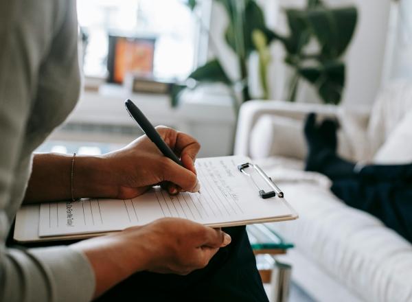 A person writes on paper using a pen and clipboard