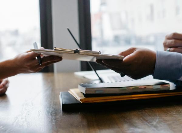 One person passes a clipboard to another across a desk