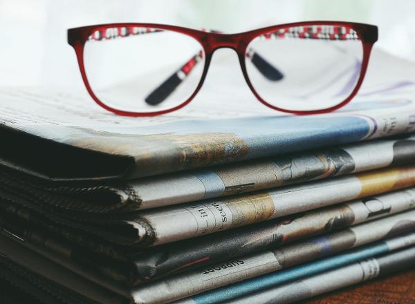 A pair of red framed eye glasses sitting on top of a stack of newspapers