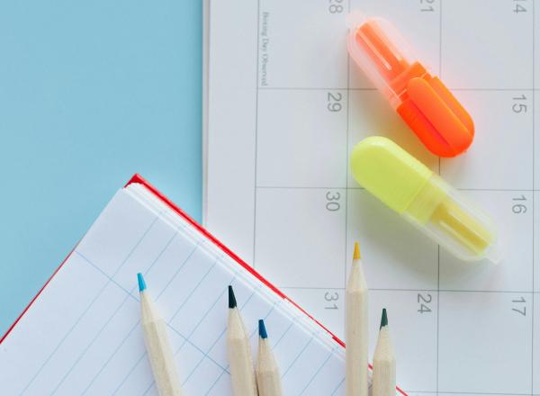 Notebook paper, pencils and highlighters sit on blue desk surface