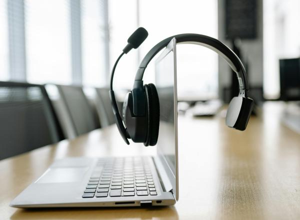 A headset hangs on a laptop, which sits on a conference table