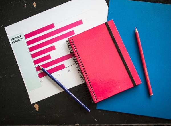 A paper bearing a bar graph, a folder, notebook and writing implements sit on a tabletop