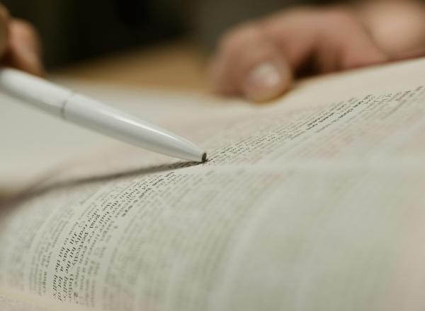 A person using a writing implement to point to a page in a book