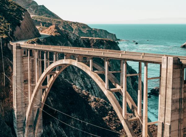 Tan bridge between a rocky cliff above teal water