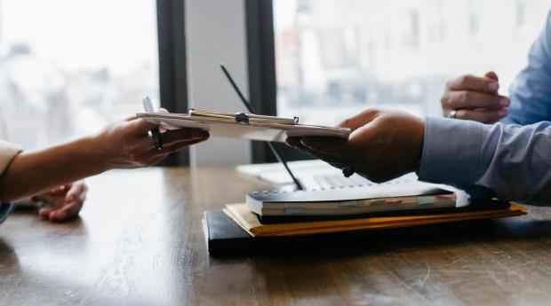 One person passes a clipboard to another across a desk