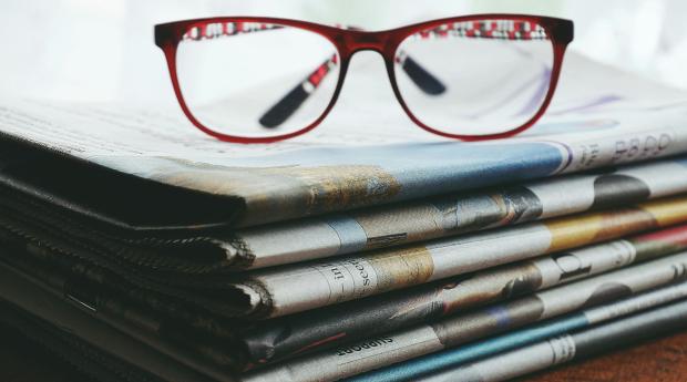 A pair of red framed eye glasses sitting on top of a stack of newspapers