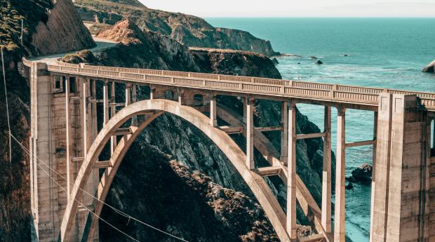 Tan bridge between a rocky cliff above teal water